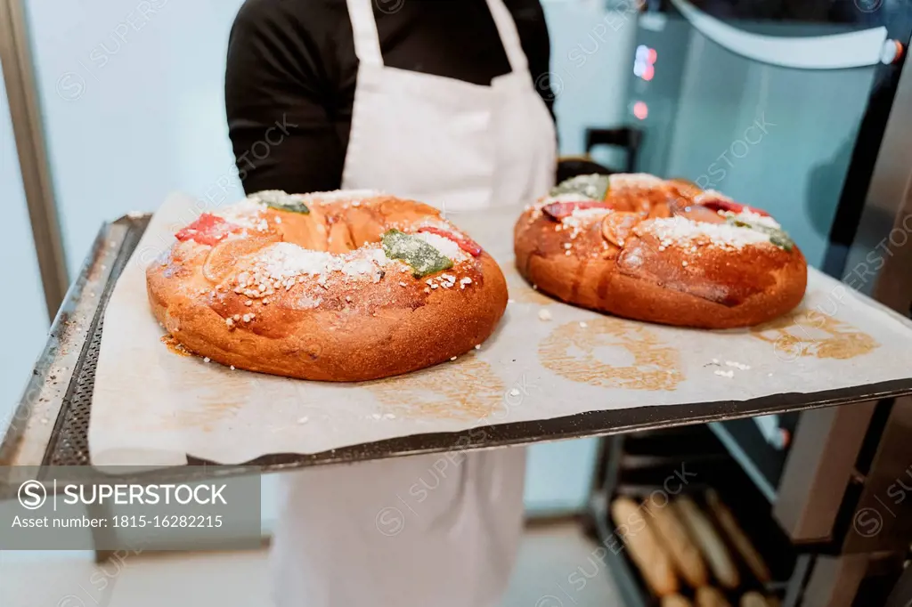 Female baker holding breads in baking tray at bakery