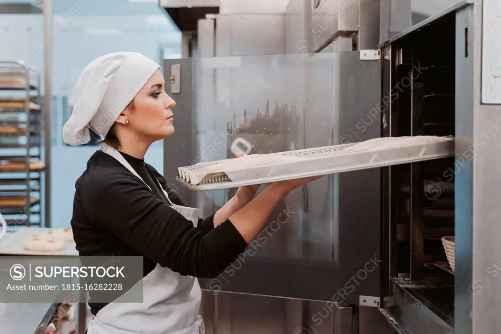 Female baker inserting baking tray in oven at bakery