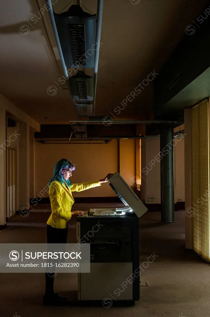 Businesswoman with dyed hair operating photocopier in old abandoned office