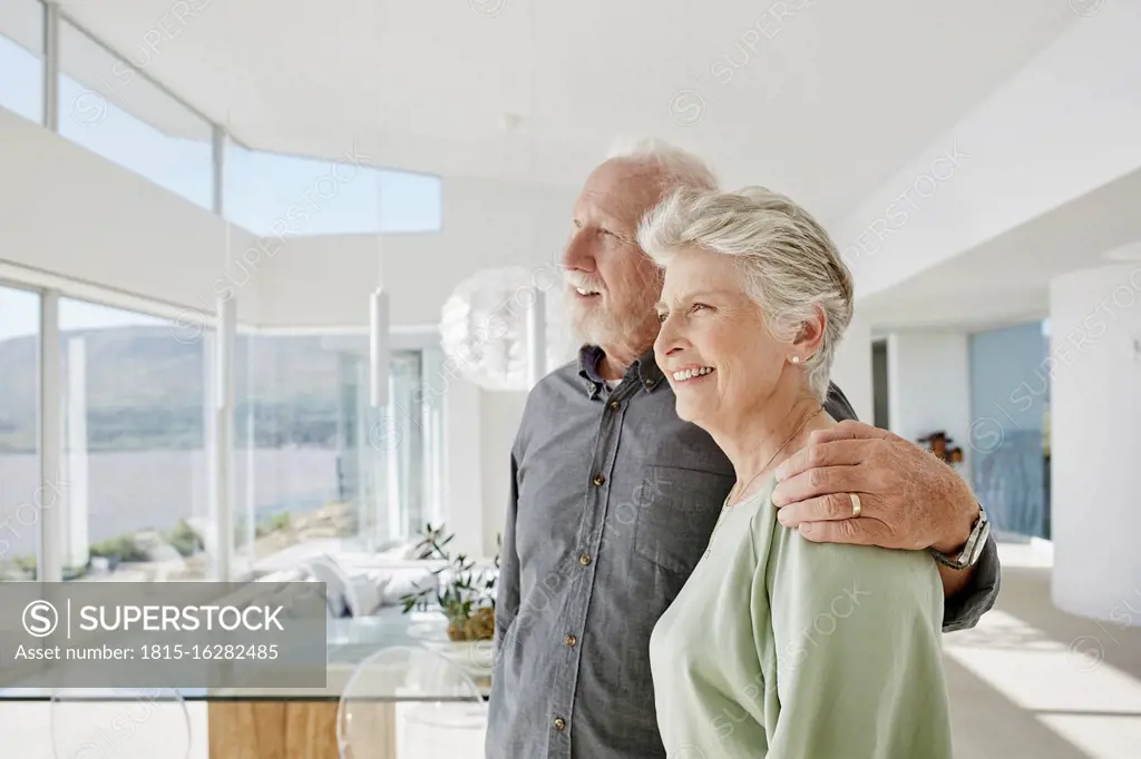 Happy senior couple in luxury beach house looking out of window