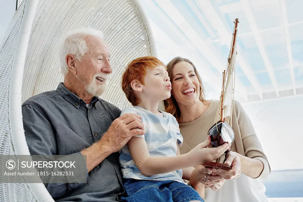 Happy grandfather, mother and son with model sailing ship in hanging chair