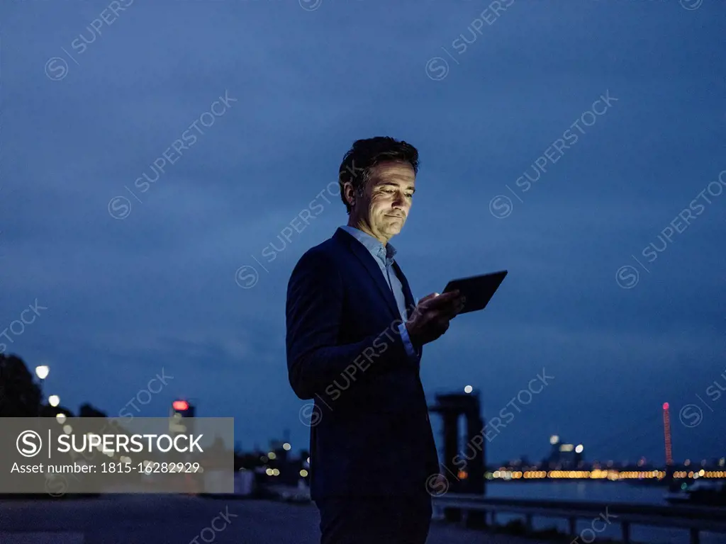 Mature businessman using tablet at the riverbank at dusk