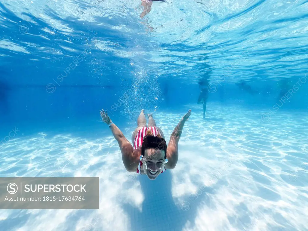 Smiling woman swimming underwater in pool at tourist resort