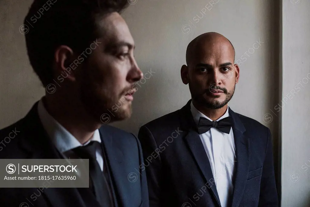 Gay couple in suits standing against wall on wedding day