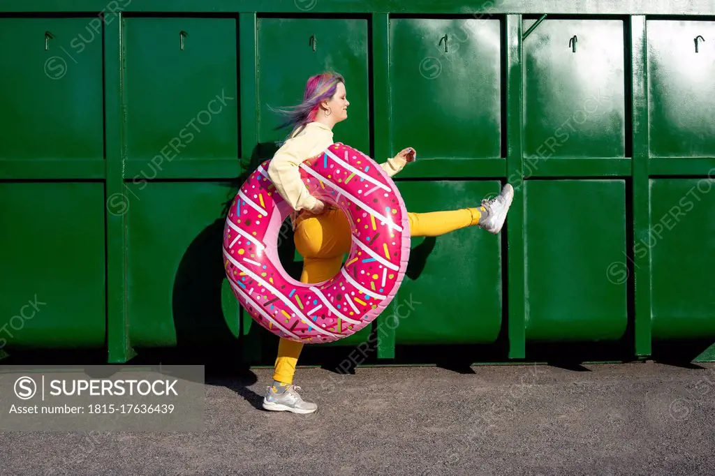 Young woman with dyed hair and floating tyre walking in front of green container