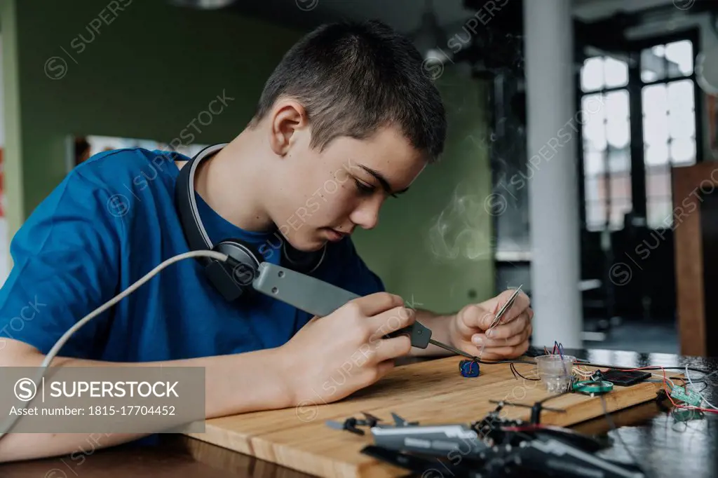 Boy sitting at home using soldering iron