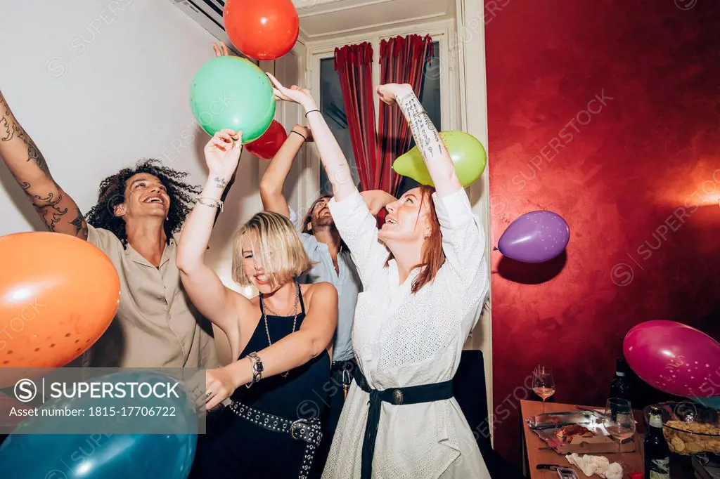 Male and female friends dancing with colorful balloons during party