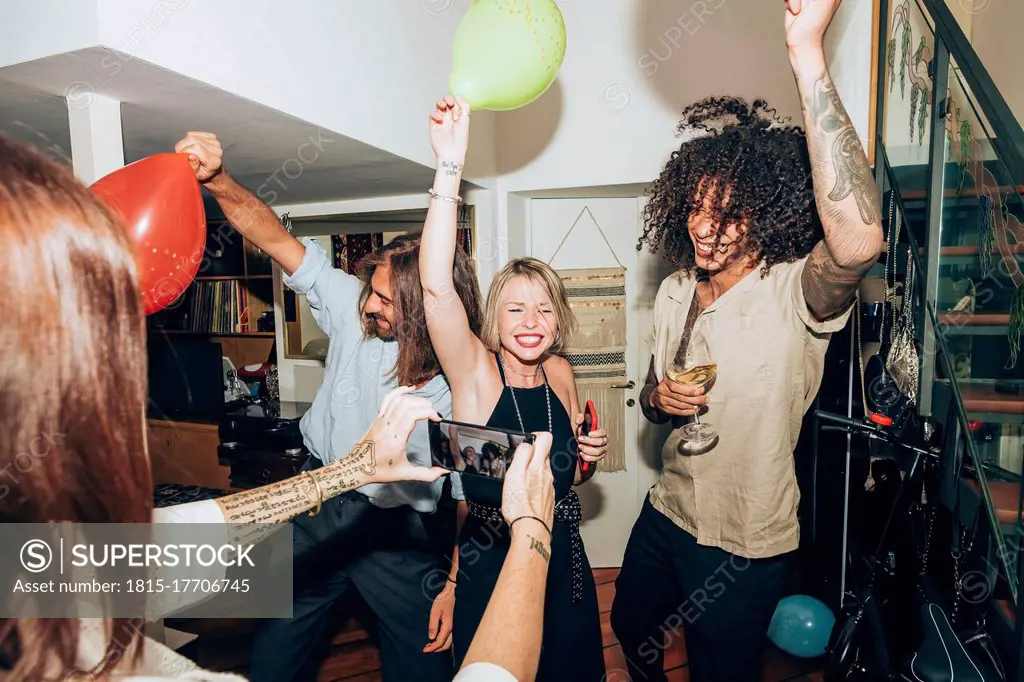 Woman photographing happy friends dancing during social gathering at home