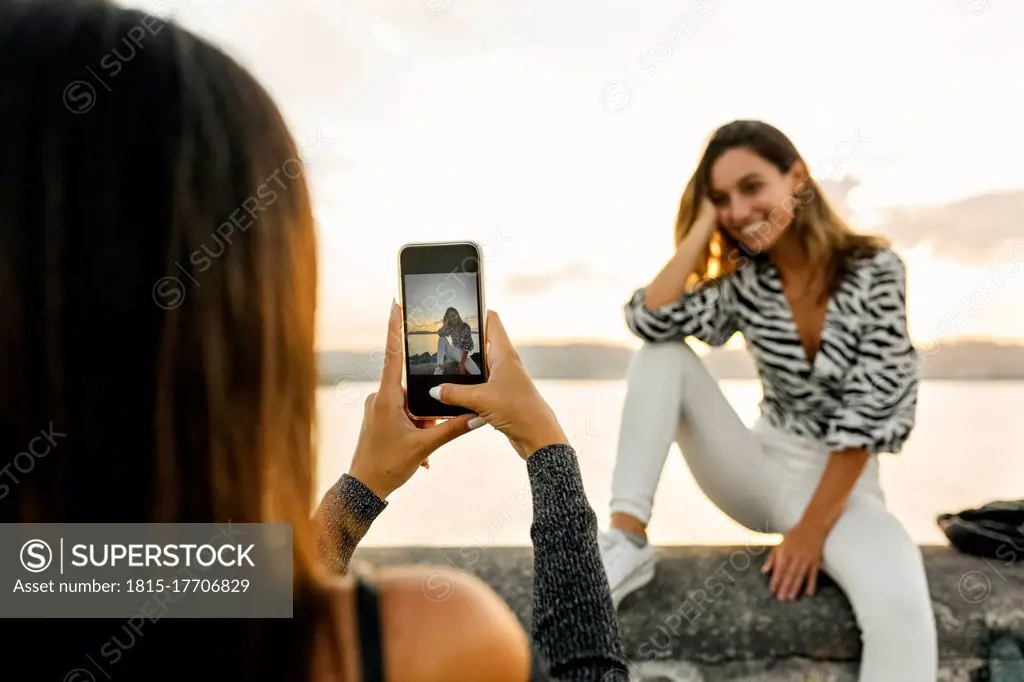 Woman taking photo of friend sitting on retaining wall at promenade