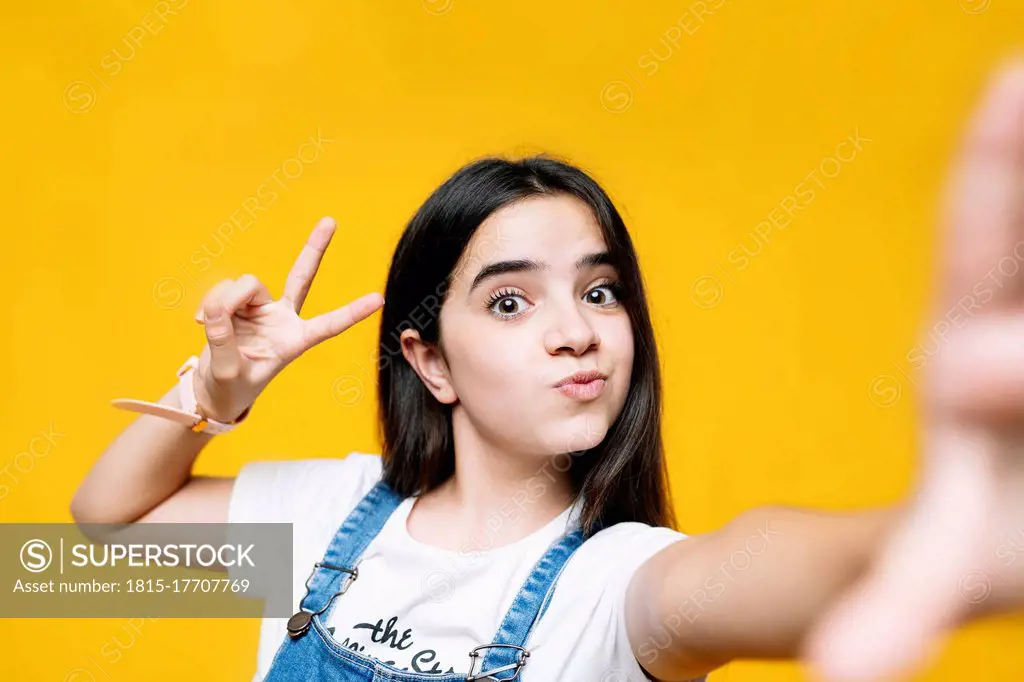 Girl showing peace sign while standing against yellow background