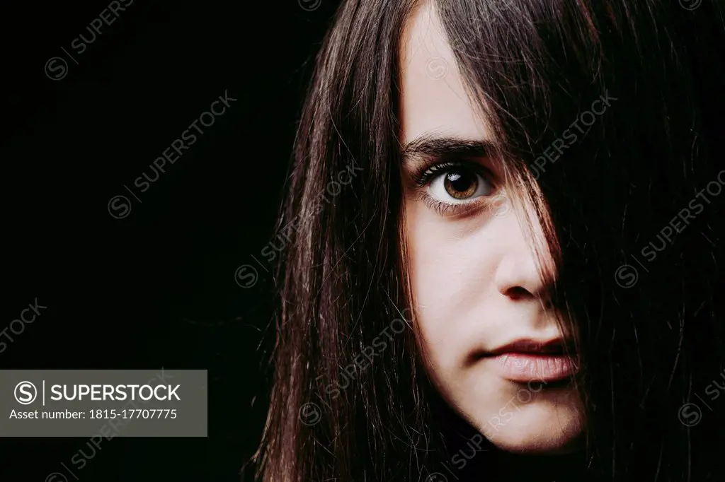 Close-up of girl with long brown hair on face against black background