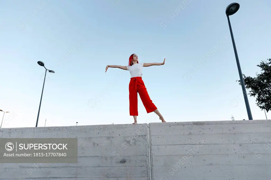 Young dancer with arms outstretched standing on surrounding wall against clear sky