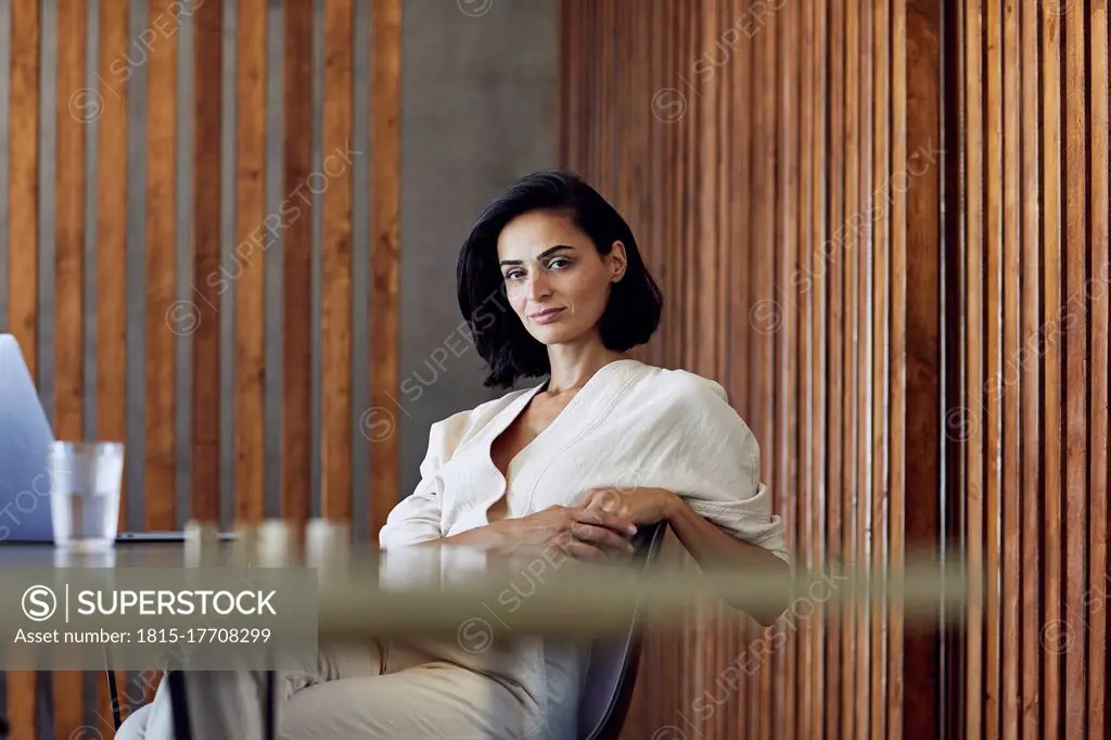 Confident female entrepreneur sitting on chair at desk in office