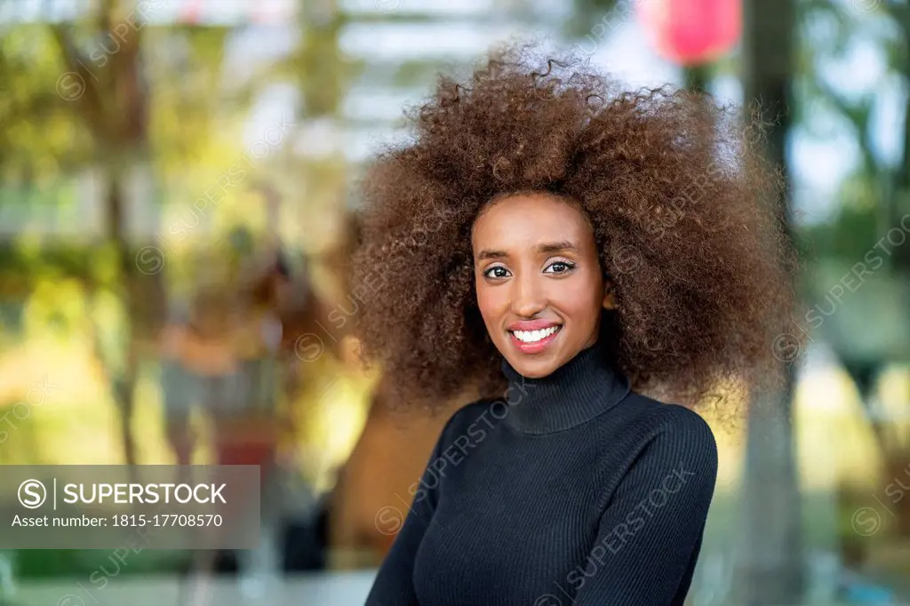 Close-up portrait of smiling businesswoman with curly frizzy hair standing outdoors