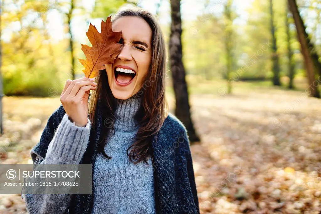 Young laughing woman holding autumn leave on her eye