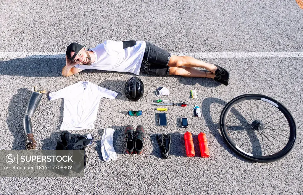 Smiling male adaptive athlete with various objects lying on road