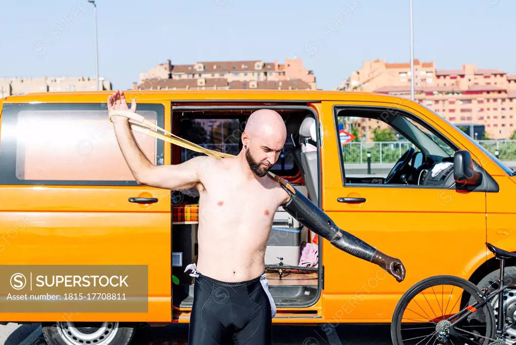 Bald adaptive athlete wearing artificial hand while standing against van