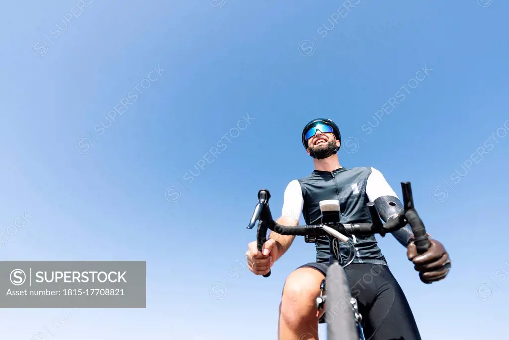 Male amputee cyclist with artificial limb riding bicycle against clear sky