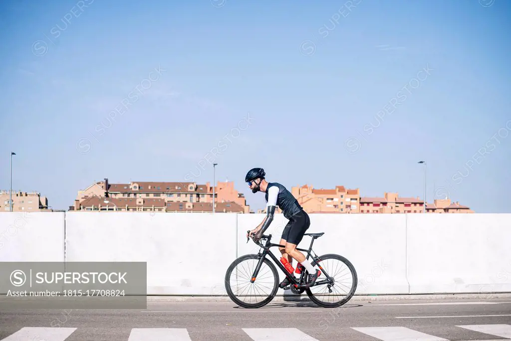 Male amputee cyclist riding bicycle on road against clear blue sky during sunny day