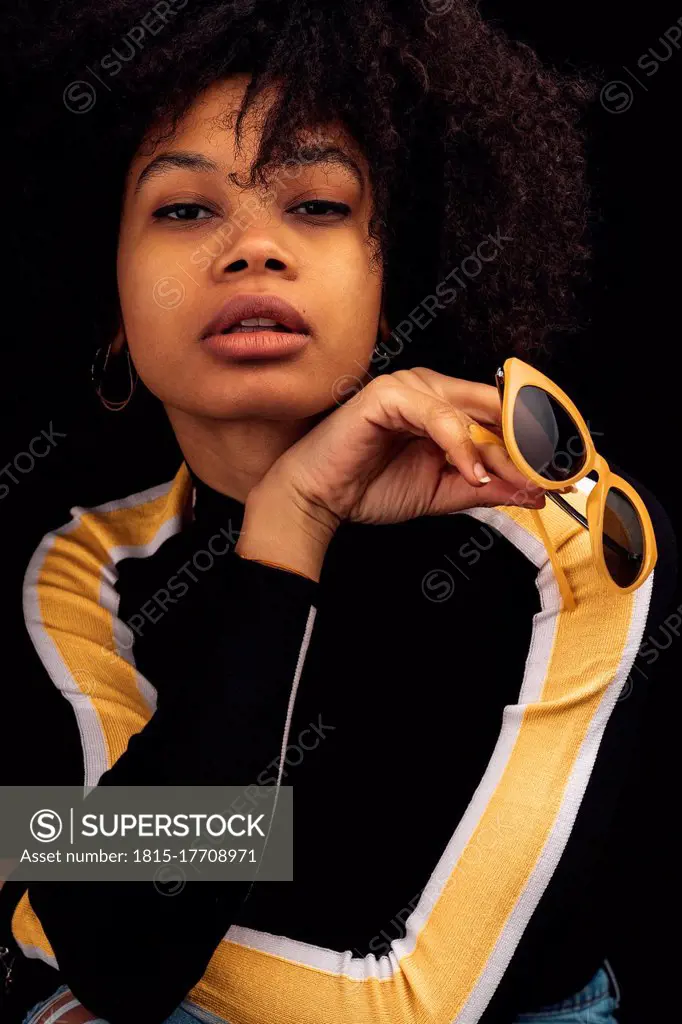 Young woman posing while holding sunglasses against black background