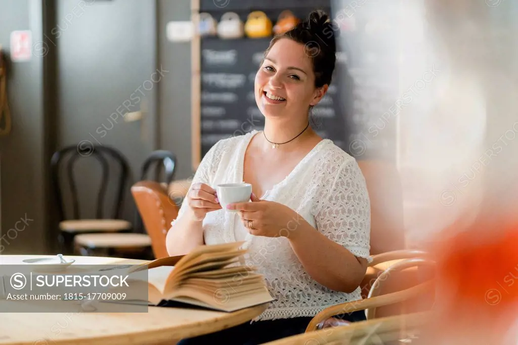 Smiling voluptuous woman holding coffee cup while sitting at table in restaurant