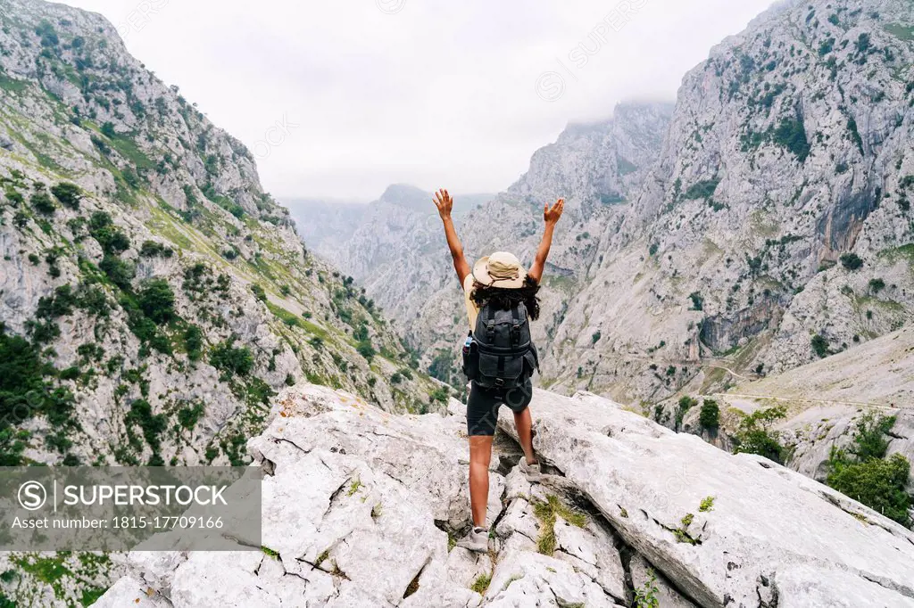 Carefree woman with hand raised standing on mountain peak at Ruta Del Cares, Asturias, Spain