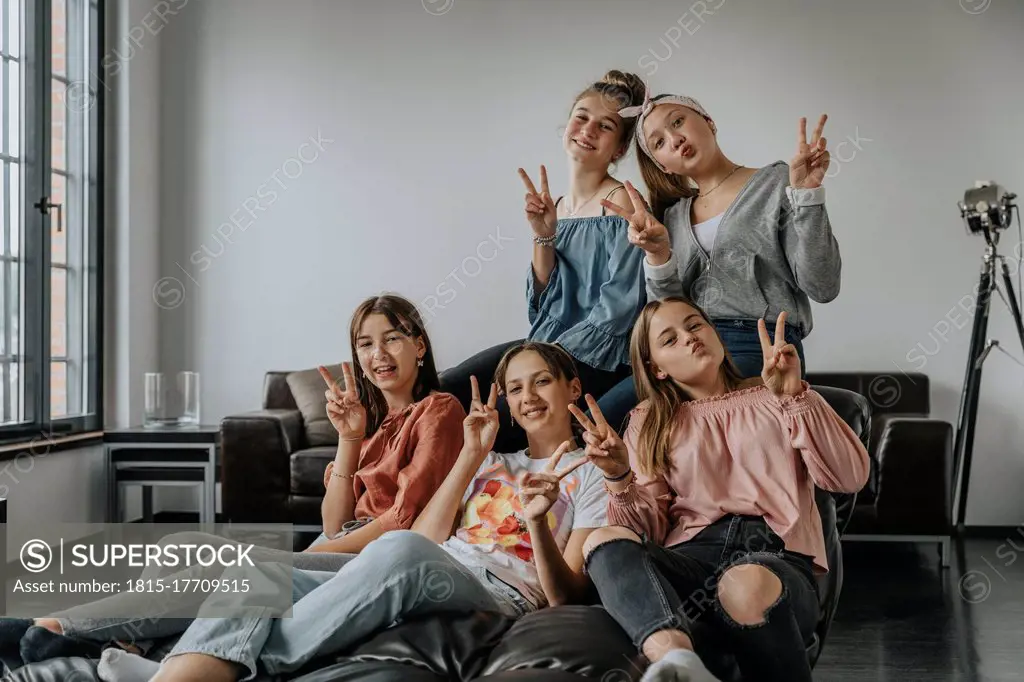 Smiling friends showing victory sign while sitting on sofa in loft apartment