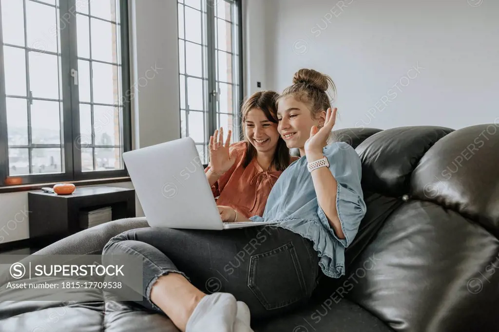 Friends waving while video conferencing over laptop on sofa at home