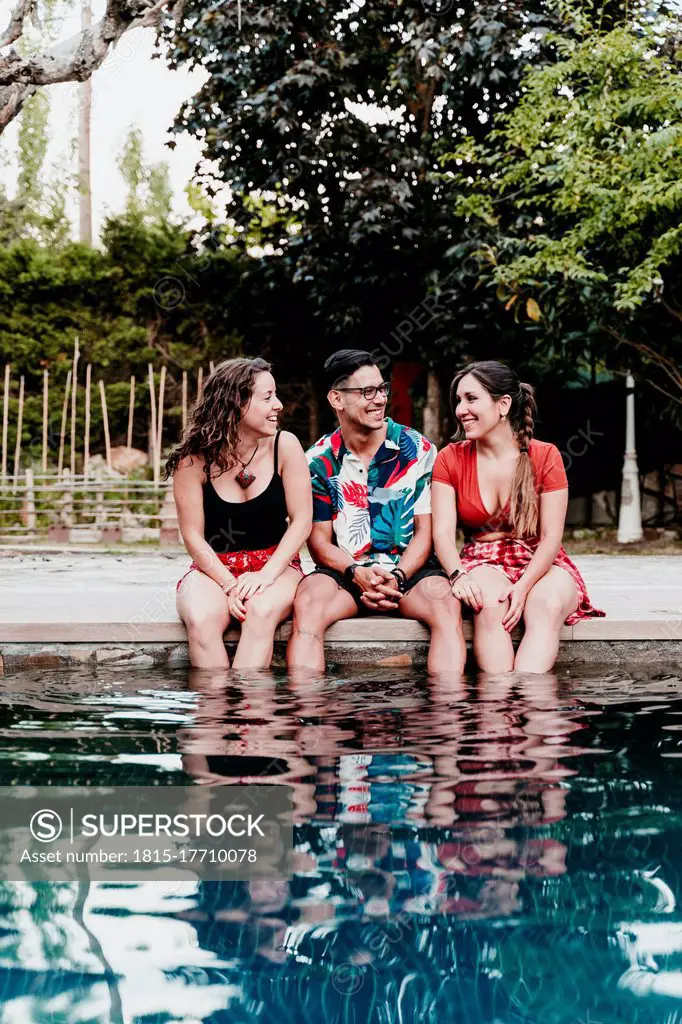 Smiling friends talking while sitting by poolside