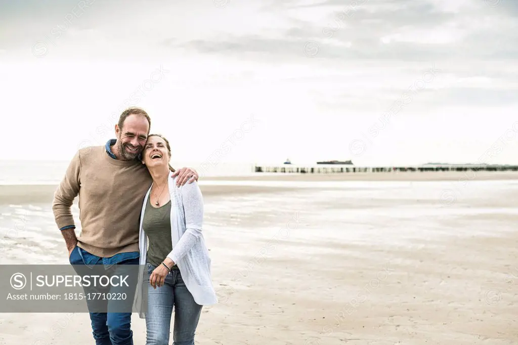 Cheerful couple laughing while walking against sea during sunset