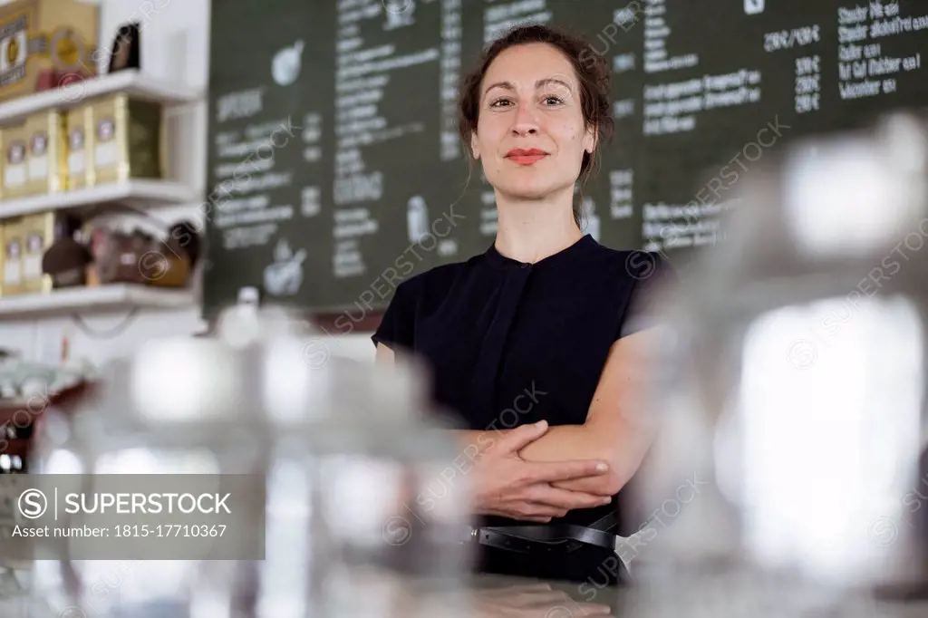 Confident female owner standing against blackboard in coffee shop