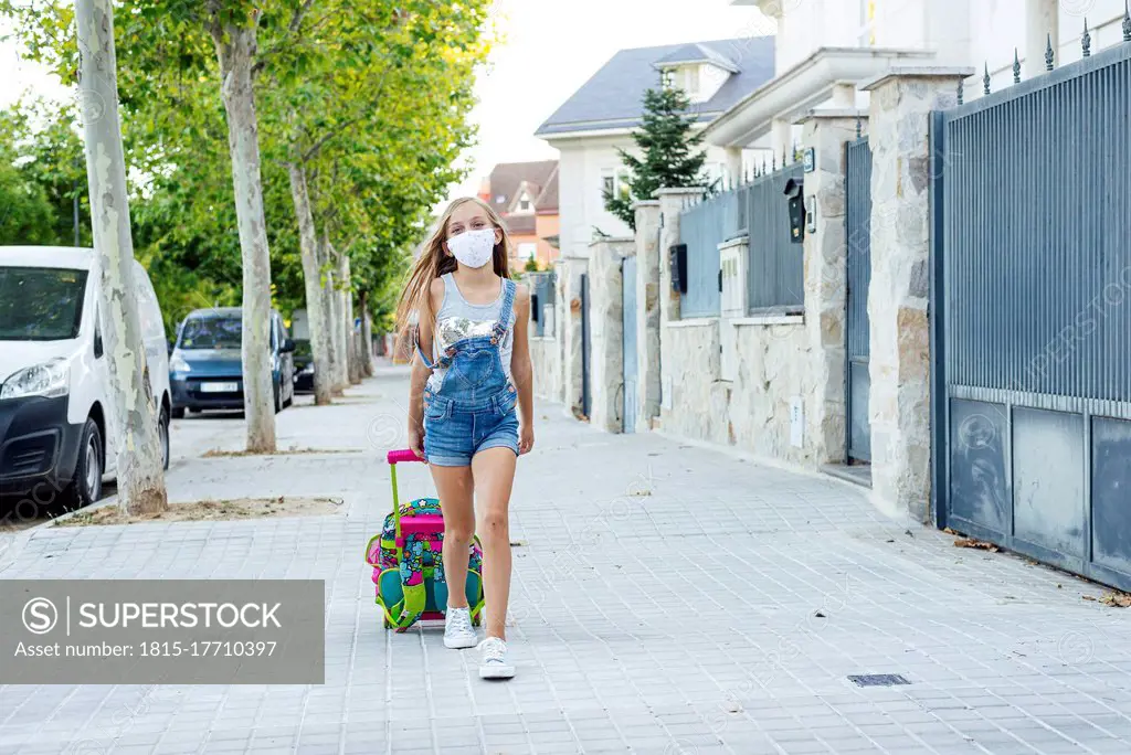 Girl with schoolbag walking on footpath wearing protective face mask