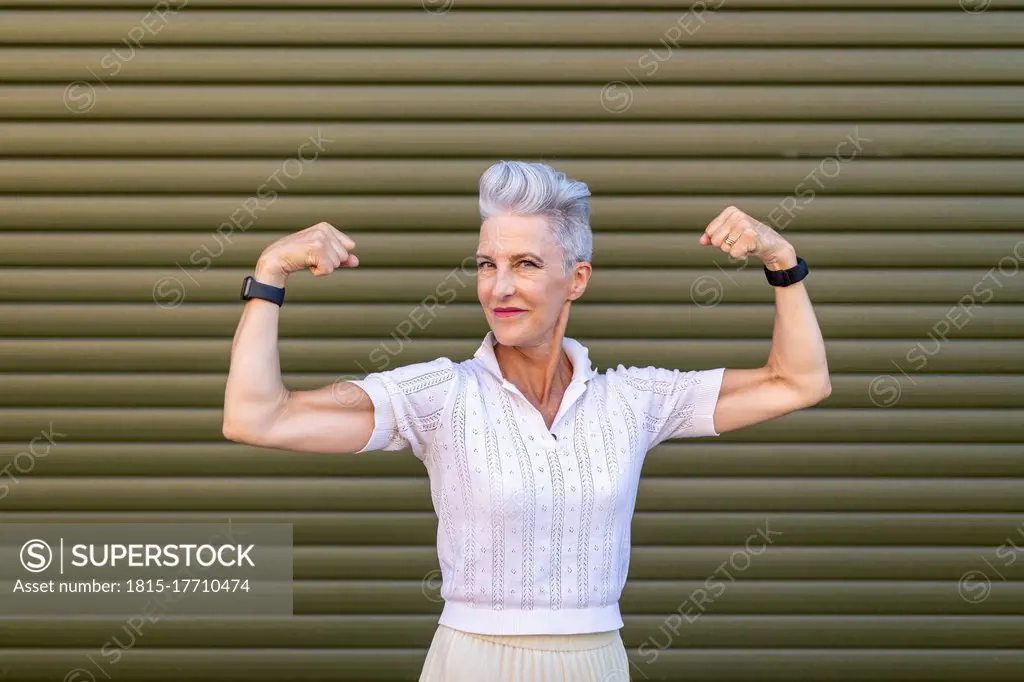 Senior woman flexing muscles while standing against shutter