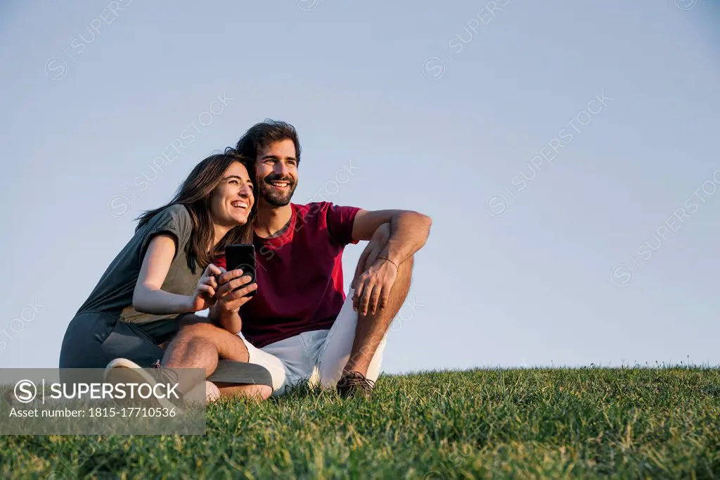 Couple sitting on grass against clear sky during sunset