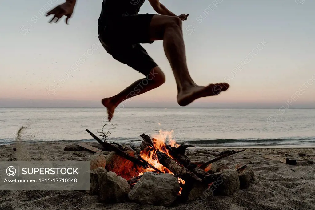 Man jumping over campfire at beach during sunset