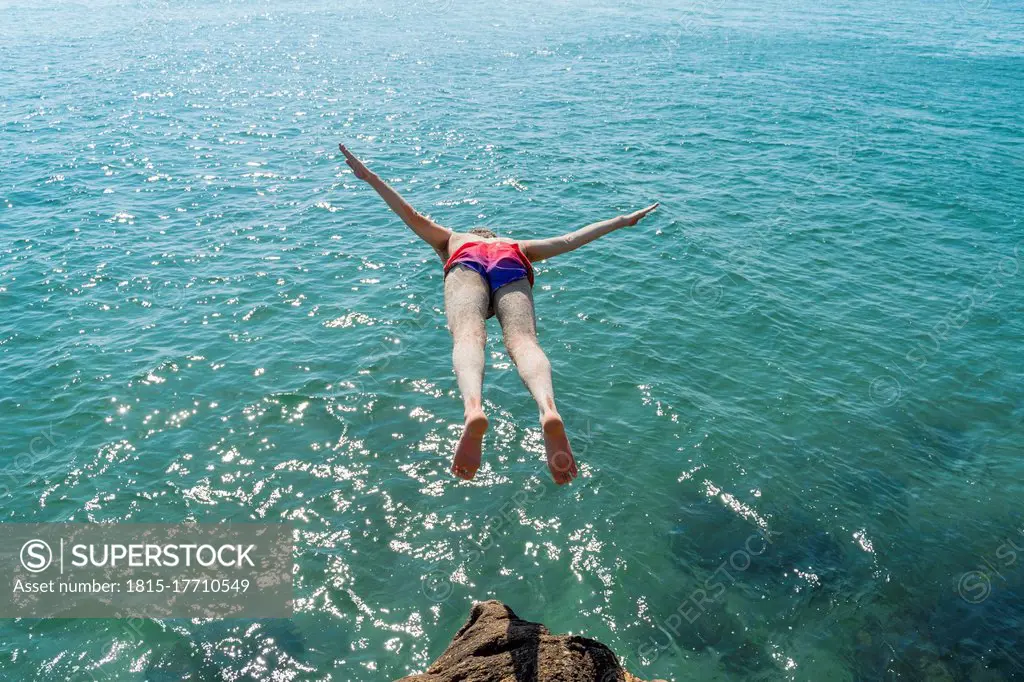 Mid adult man jumping into sea on sunny day