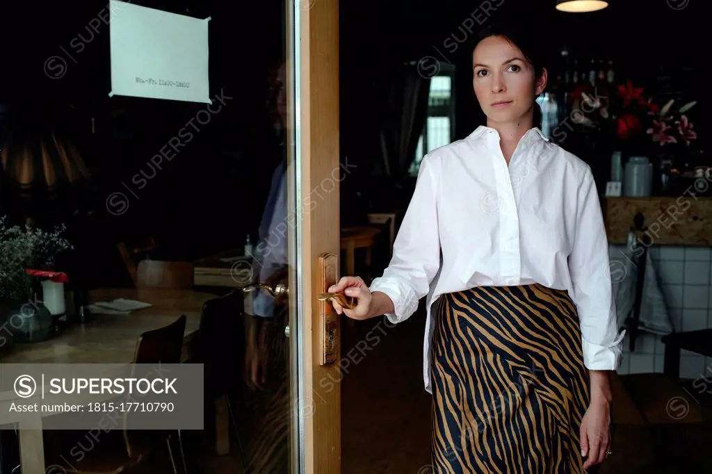 Portrait of female owner standing at entrance in coffee shop