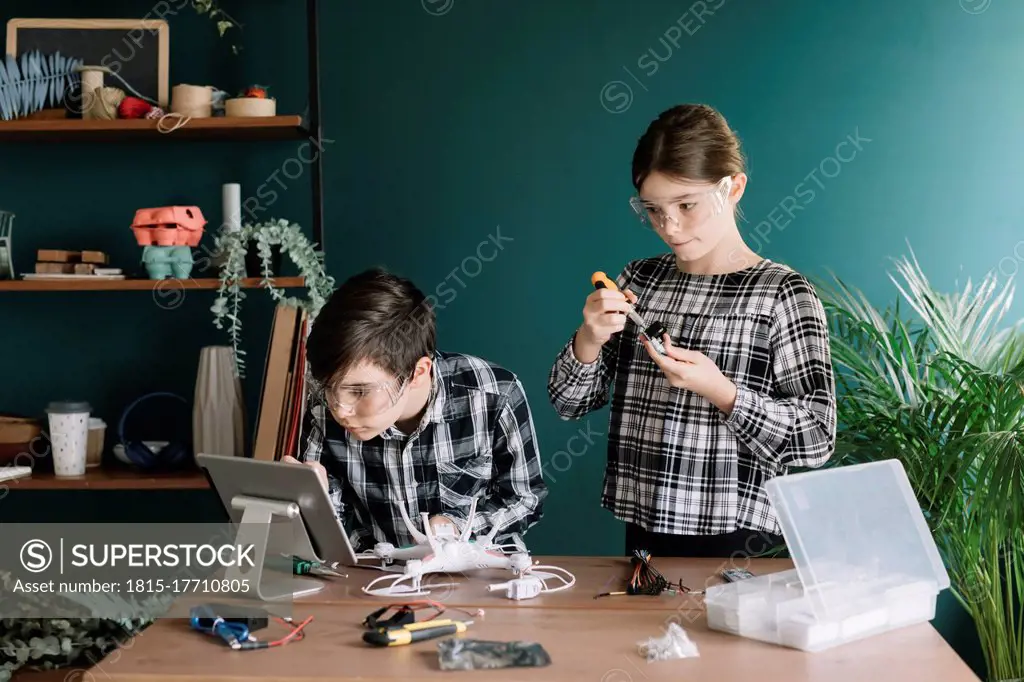 Siblings using digital tablet while preparing drone on table against wall at home