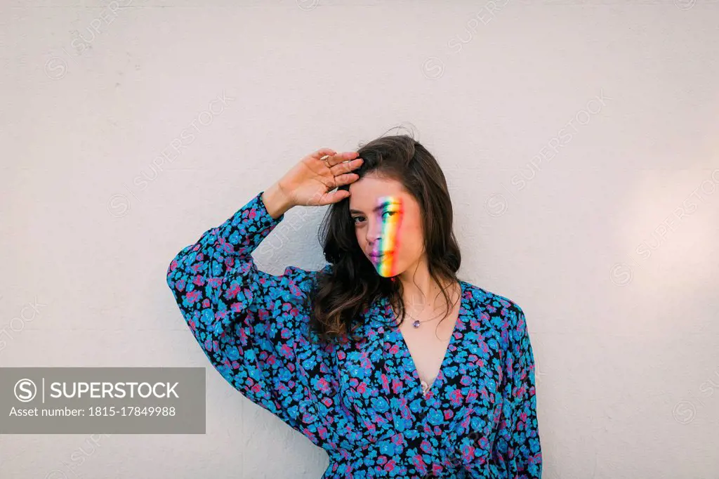 Young woman with prism light on face standing against white wall