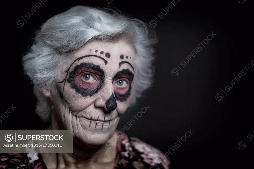 Portrait of senior woman with sugar skull make-up in front of black background