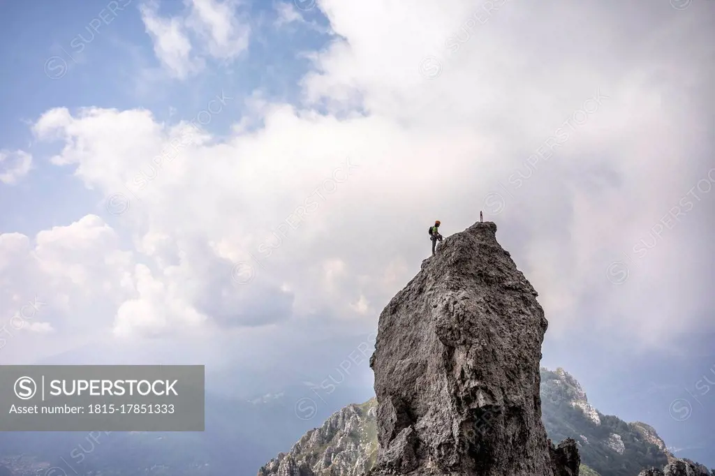 Male hiker standing on top of mountain against cloudy sky, European Alps, Lecco, Italy