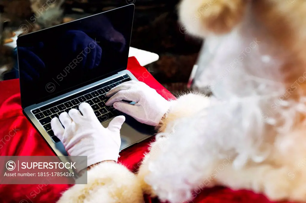 Man wearing Santa Claus costume using laptop while sitting at home