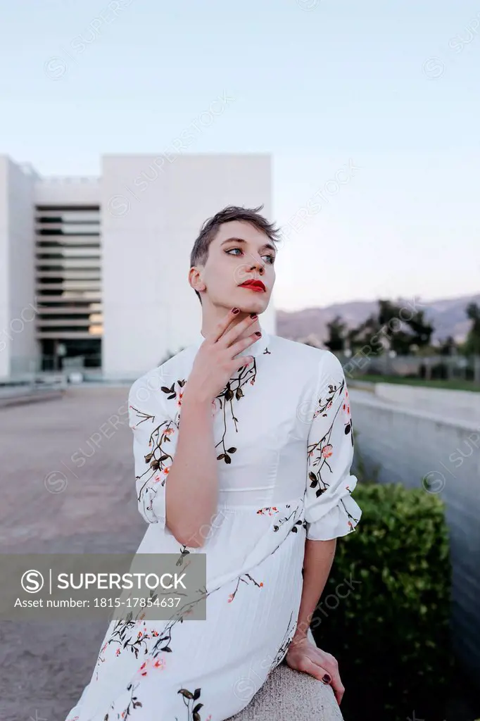 Contemplating gender fluid man sitting on retaining wall