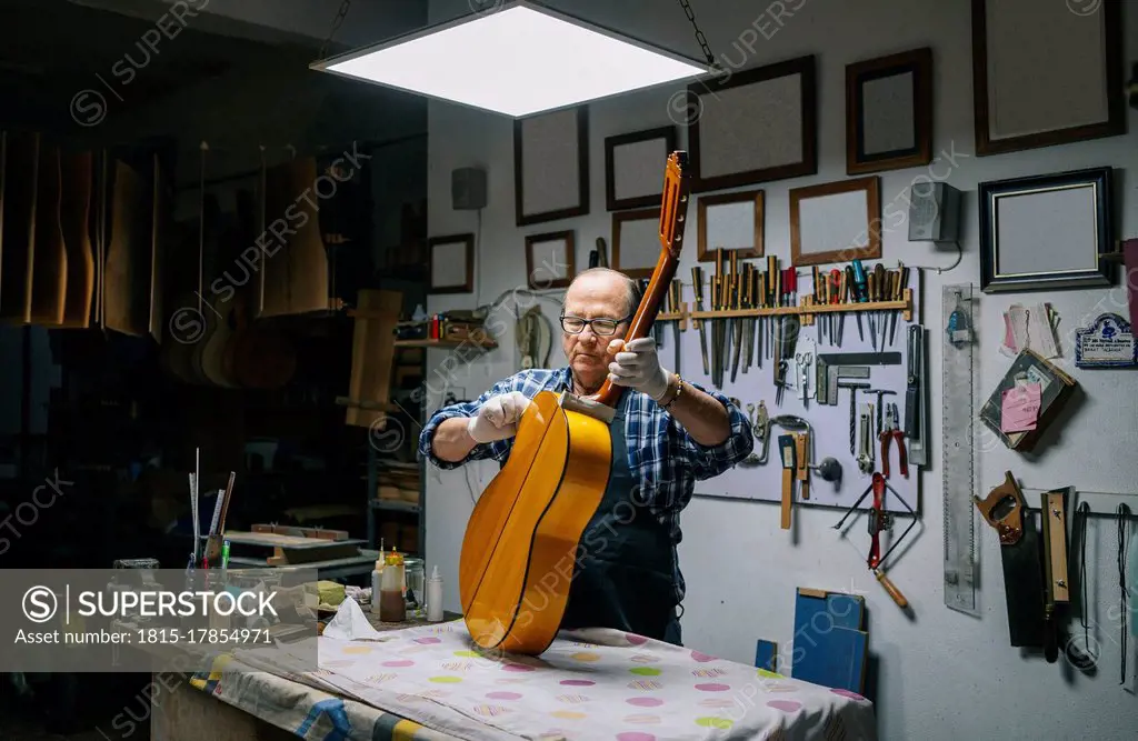 Man holding guitar on workbench while working at workshop