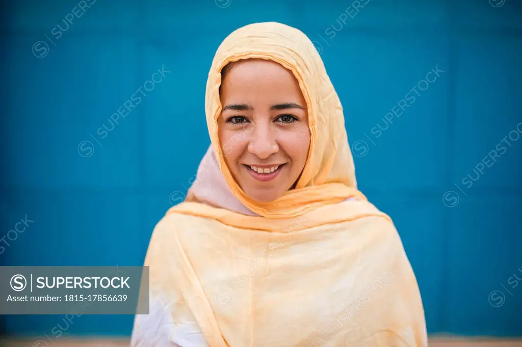 Young smiling woman standing against blue wall