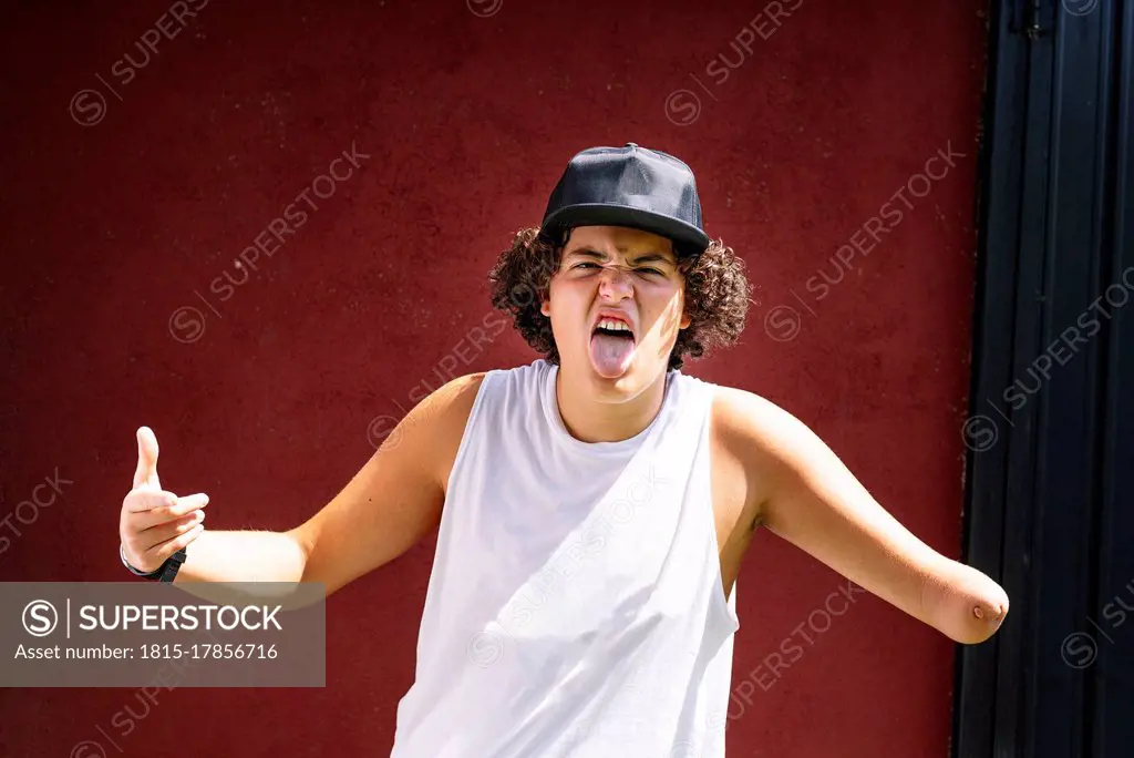 Amputee boy sticking out tongue while standing against brown wall