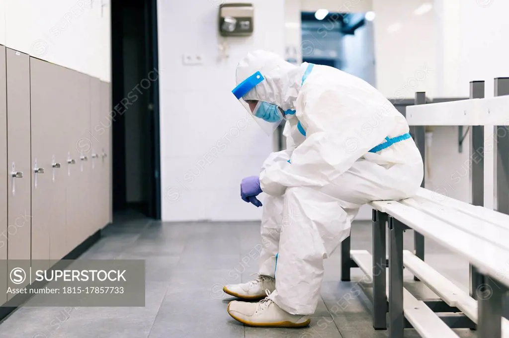 Thoughtful man wearing protective suit sitting on bench in hospital