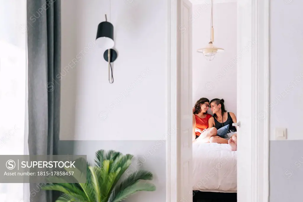 Smiling female friends sitting on bed in bedroom