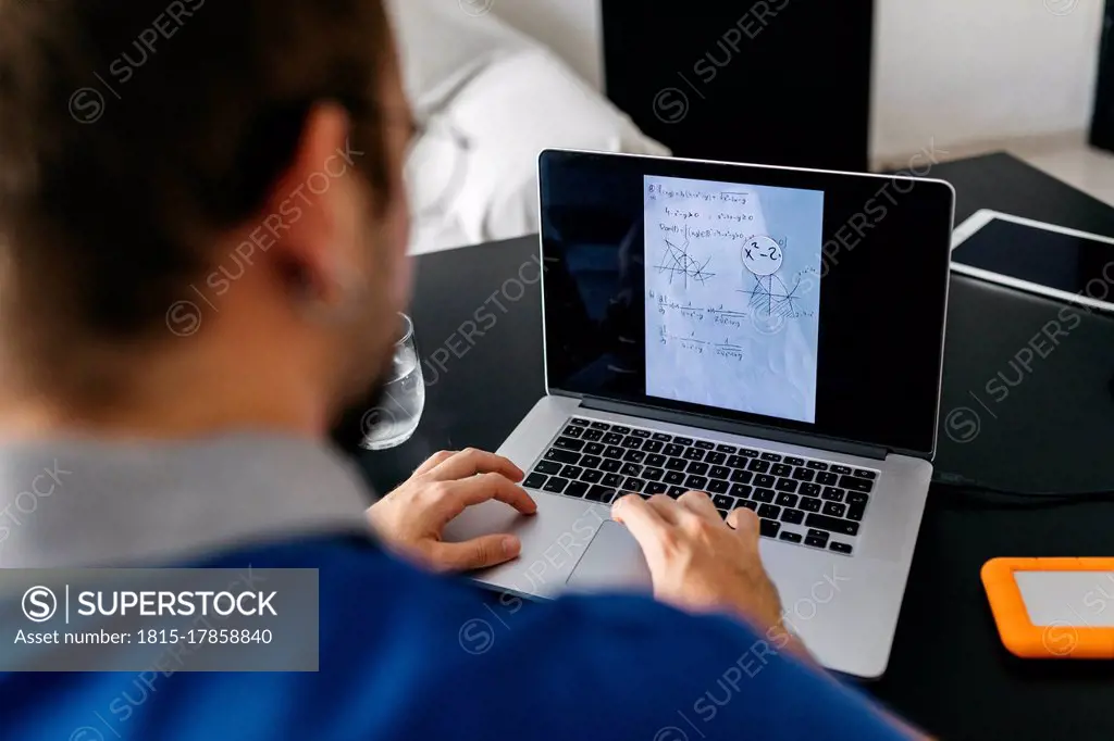 Adult male student doing mathematics homework through laptop at home