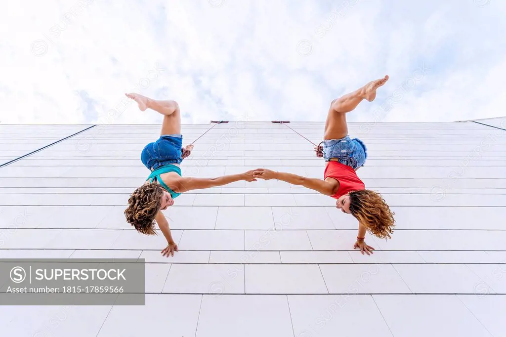 Aerial dancers upside down holding hands while hanging on window